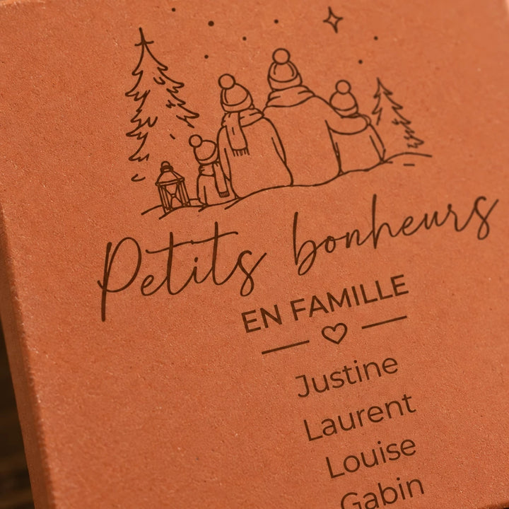 Gros plan sur la famille devant les sapins et les prénoms Justine, Laurent, Louise et Gabin gravés.