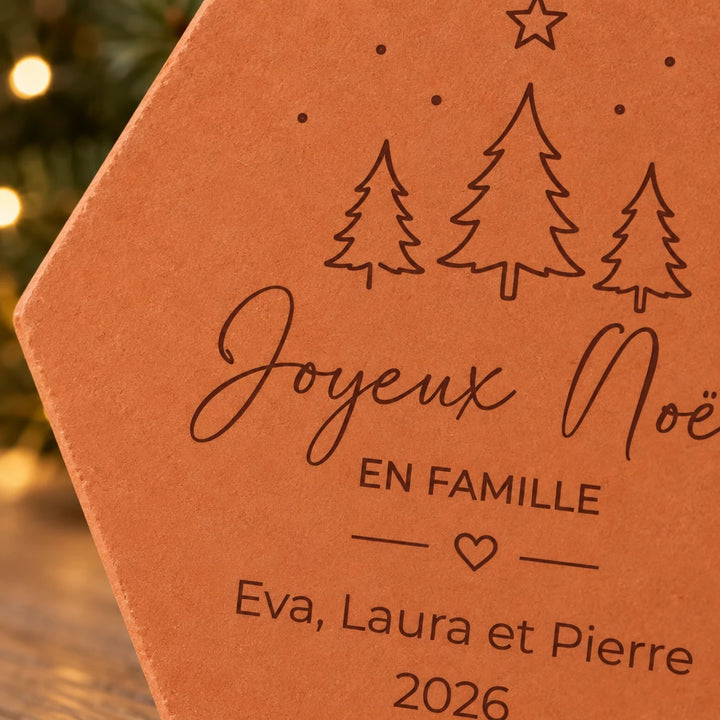 Détail des sapins, du cœur et des prénoms Eva, Laura et Pierre gravés sur la tomette de Noël.