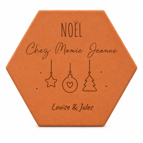 Pieza hexagonal de terracota grabada con adornos de estrella, bola y abeto, «Noël chez Mamie Jeanne», Louise y Jules, sobre fondo blanco.