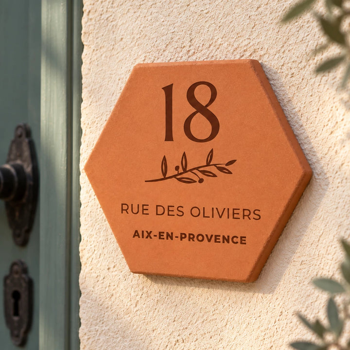 Personalised house plaque engraved with “18 rue des Oliviers”, “Aix-en-Provence” and a branch, shown close up on the wall, with the number 18 and leafy sprig clearly visible.