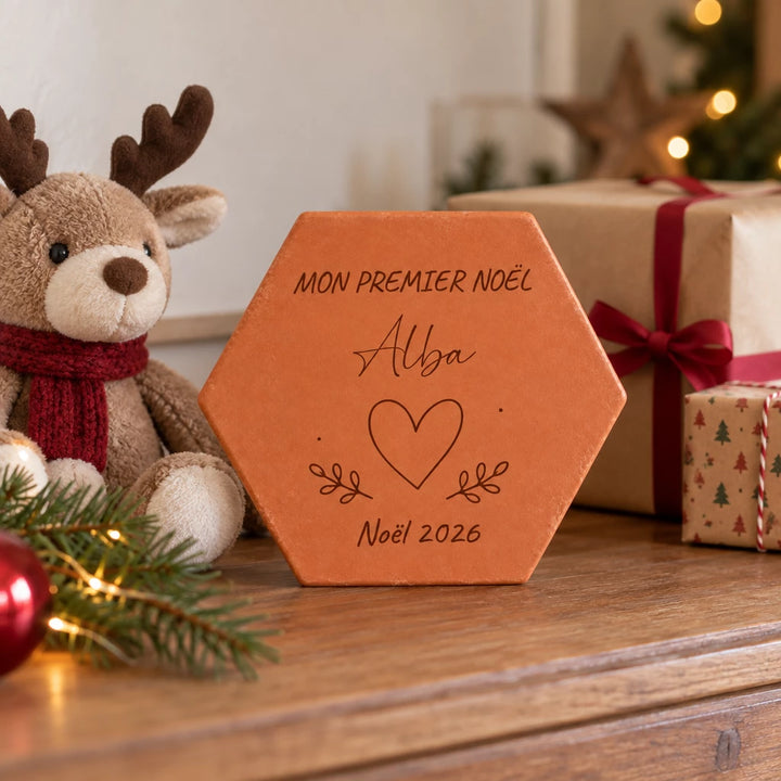Tomette personnalisée « Mon premier Noël », Alba, cœur et année gravés, près d’un renne en peluche et de cadeaux emballés.