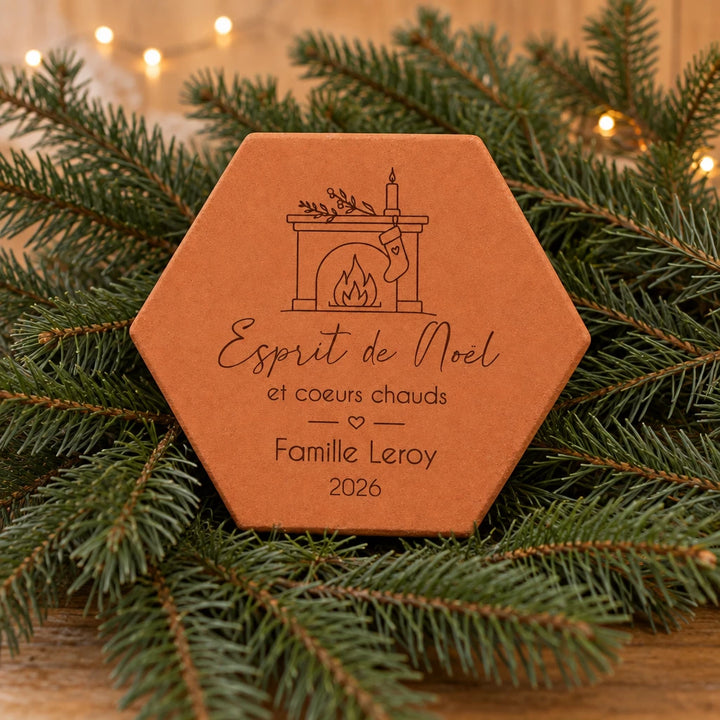Tomette personnalisée « Esprit de Noël », Famille Leroy et cheminée gravés, nichée dans des branches de sapin avec une guirlande lumineuse.