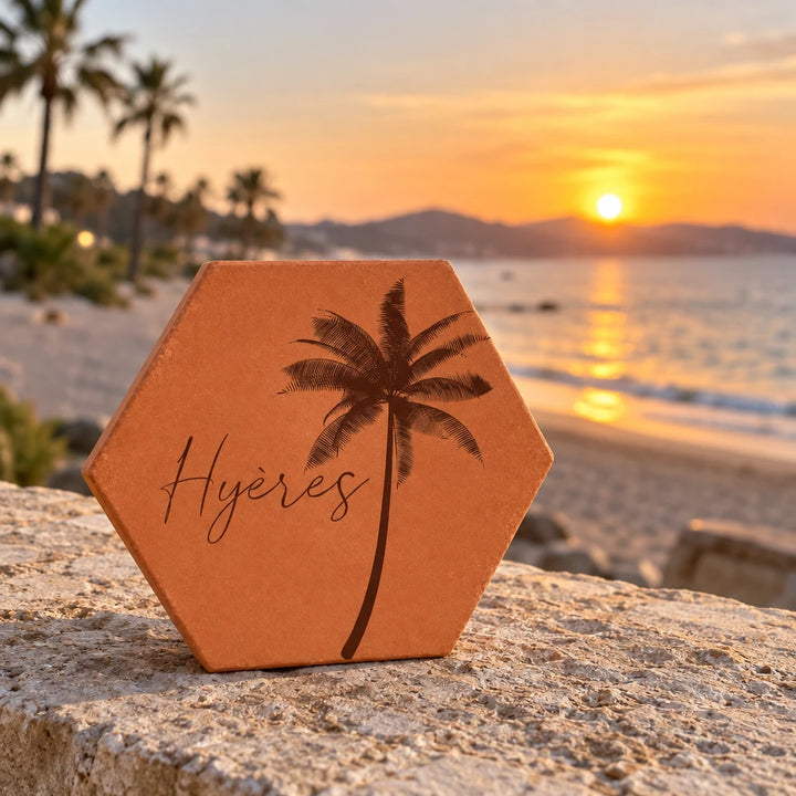 Tomette souvenir personnalisée « Hyères » avec palmier gravé, sur un muret face à la mer au coucher du soleil.