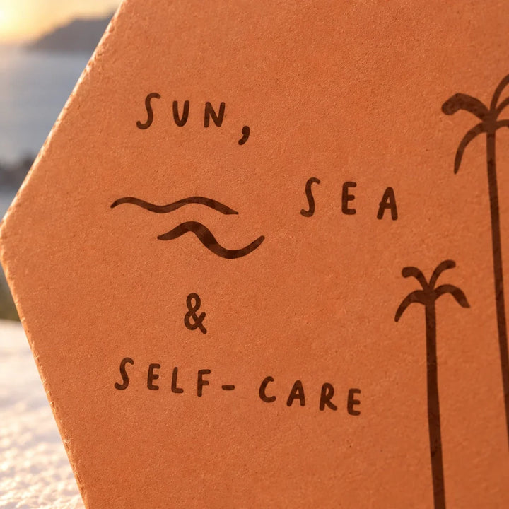 Gros plan sur les lettres Sun, sea & self-care, les vagues et les palmiers gravés.