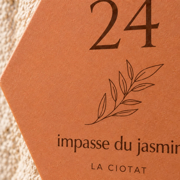 Gros plan sur le numéro 24, le rameau et l’adresse gravés sur la plaque.
