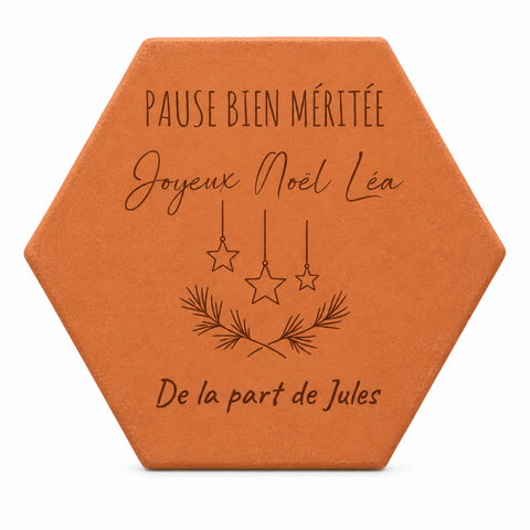 Pieza hexagonal de terracota grabada con estrellas, ramas, «Pause bien méritée» y «Joyeux Noël Léa, de la part de Jules», sobre fondo blanco.