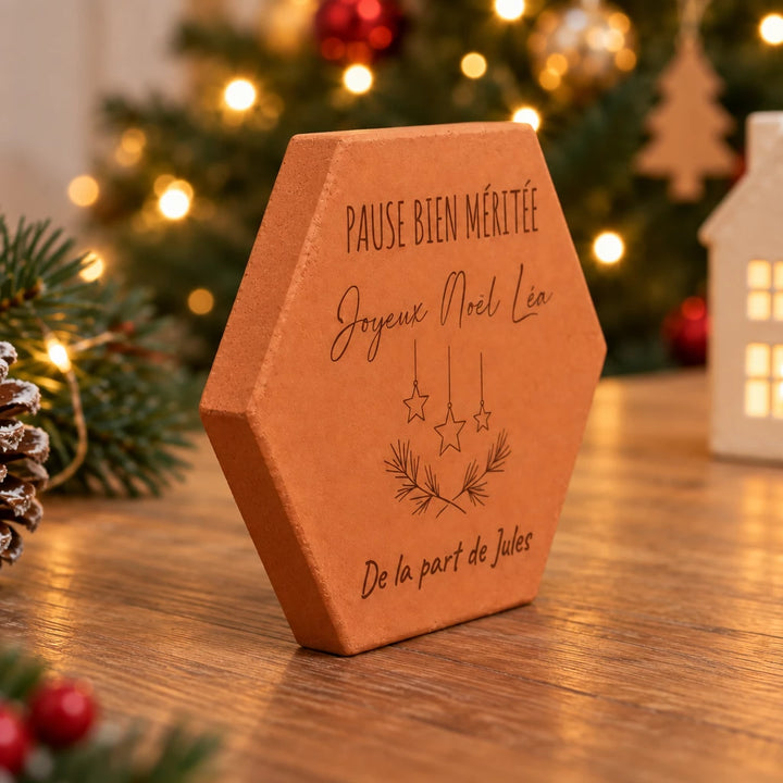 Tomette de Noël pour la maîtresse vue de profil sur une table en bois, devant le sapin illuminé.