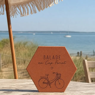 Tomette hexagonale gravée « Balade au Cap Ferret » et un vélo, posée face à la mer