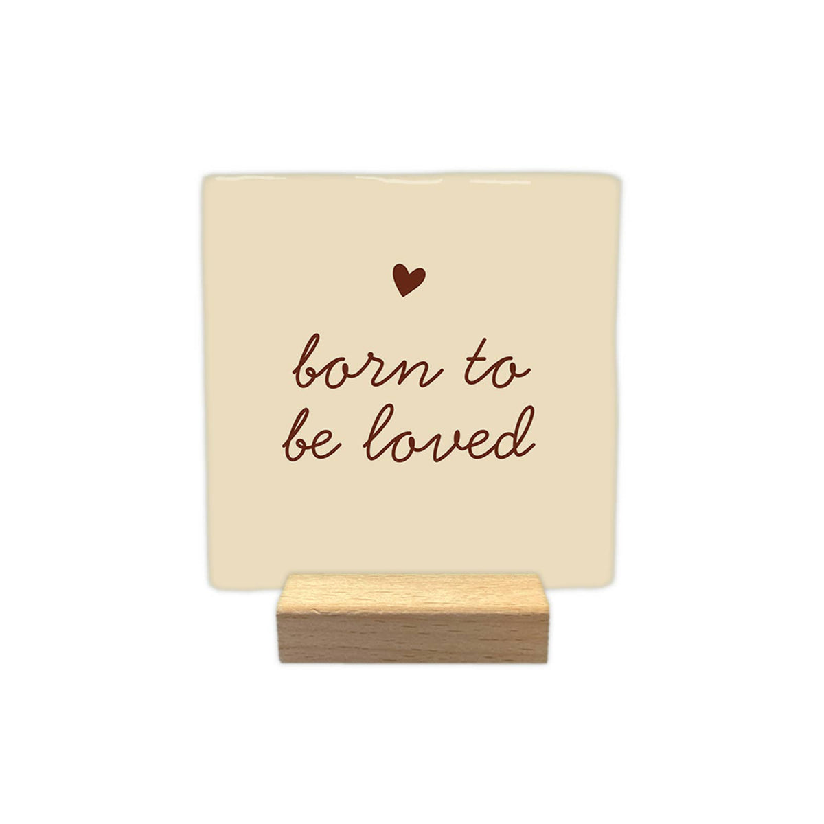 Carreau décoratif crème « born to be loved » avec cœur brun, présenté sur un petit support en bois sur fond blanc.