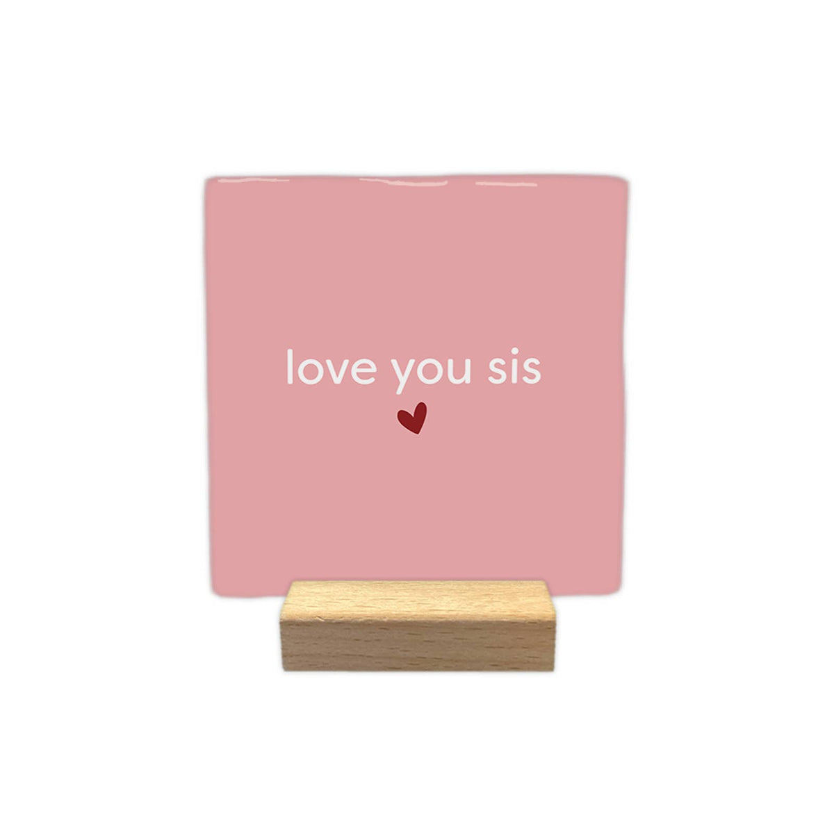 Pink “love you sis” decorative tile with a small red heart, displayed on a small wooden stand against a white background.