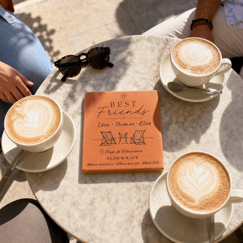 Carreau d’amitié personnalisé « Best Friends », trois prénoms, transats et lieu gravés, vu du dessus sur une table de café entourée de trois tasses.