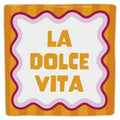 “La Dolce Vita” decorative tile, with yellow lettering and a wavy pink border on orange stripes, viewed from the front against a white background.