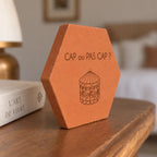 Tomette gravée « Cap ou pas cap ? » avec carrousel, vue de côté sur une table en bois près d’un livre.