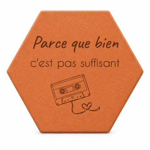 Hexagonal terracotta tile engraved with “Parce que bien c'est pas suffisant” — white background.