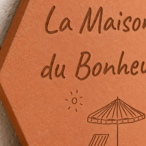 Détail de la tomette Maison du Bonheur : lettres gravées, soleil et parasol.
