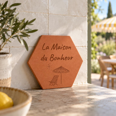 Tomette gravée « La Maison du Bonheur », parasol et chaise longue, adossée à un mur près d’une branche d’olivier et d’une coupelle de citrons.