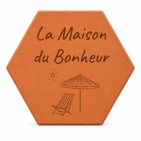 Cadeau de crémaillère porte-bonheur : tomette gravée « La Maison du Bonheur », parasol et chaise longue, sur fond blanc.