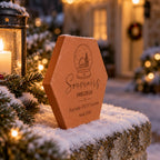 Tomette de Noël personnalisée « Souvenirs précieux », Famille Petit et boule à neige gravées, vue de côté sur le muret enneigé près de branches illuminées.