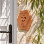 Personalised “Quai des Embruns, Cassis” house plaque, engraved with the number 27 and a small boat, viewed from the side beside the white door beneath foliage.
