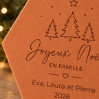 Détail des sapins, du cœur et des prénoms Eva, Laura et Pierre gravés sur la tomette de Noël.