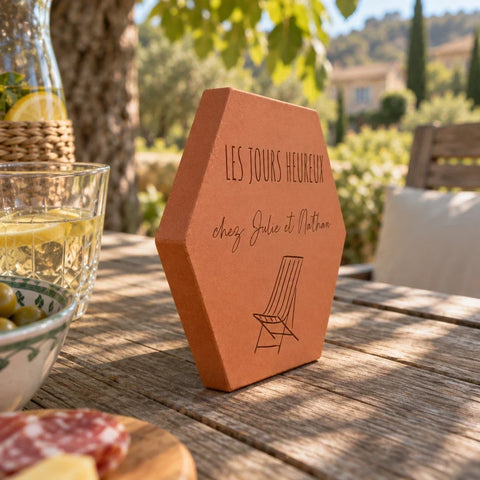 Tomette personnalisée « Les jours heureux chez Julie et Nathan » et chaise longue gravées, vue de côté sur la table dressée à l’ombre d’un arbre.