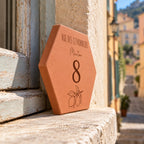 Personalised plaque engraved with “8 rue des Citronniers”, “Menton” and a lemon branch, viewed from the side on the sill beside an old window.