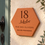 Personalised house plaque engraved with “18 rue des Oliviers”, “Aix-en-Provence” and a branch, shown close up on the wall, with the number 18 and leafy sprig clearly visible.