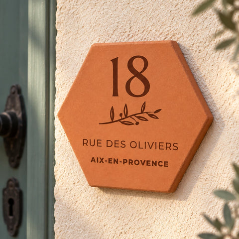 Personalised house plaque engraved with “18 rue des Oliviers”, “Aix-en-Provence” and a branch, shown close up on the wall, with the number 18 and leafy sprig clearly visible.