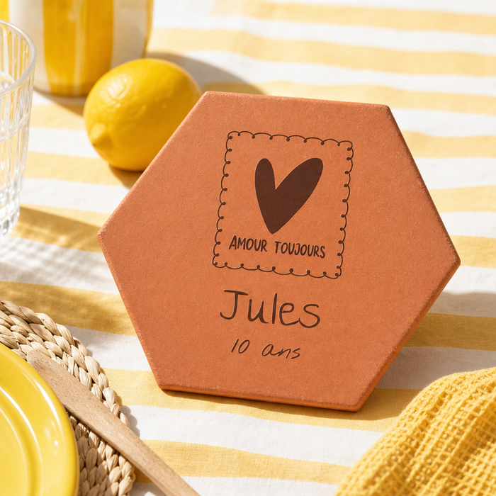Cadeau de naissance : tomette hexagonale personnalisée en terre cuite de Salernes gravée au laser sur table d'été jaune.