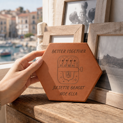 Tomette personnalisée « Better Together », quatre sardines et prénoms gravés, tenue en main devant des cadres photo et un port.