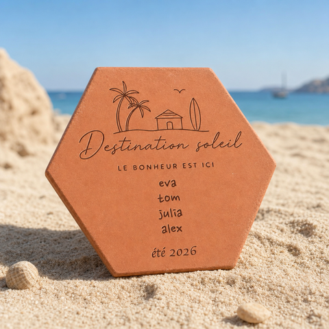 Tomette souvenir personnalisée « Destination soleil », quatre prénoms et été 2026 gravés, dressée dans le sable devant la mer.