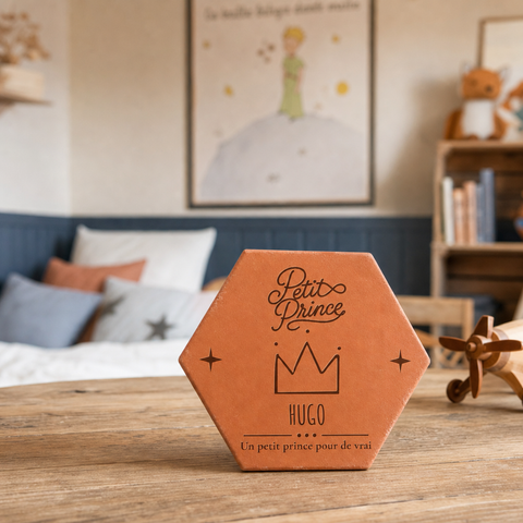Tomette personnalisée « Petit Prince », Hugo et couronne gravés, sur une table en bois devant un canapé et une affiche.
