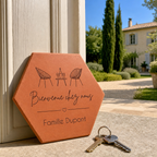 Cadeau crémaillère avec tomette hexagonale personnalisée, terre cuite de Salernes gravée au laser, terrasse et maison provençale floutées.