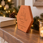 Tomette de Noël personnalisée « Joyeux Noël en famille », trois prénoms et sapins gravés, vue de côté près d’un livre et d’un photophore étoilé.