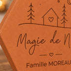 Gros plan sur la maison à cœur, les sapins et le nom Famille Moreau gravés.