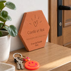 Tomette personnalisée « Notre premier chez-nous », Camille et Noé, cœur et adresse gravés, vue de biais près de clés et d’une porte en bois.