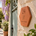 Plaque de maison personnalisée 24 impasse du Jasmin, La Ciotat et brindille gravés, vue de côté sur le mur près du portail fleuri.