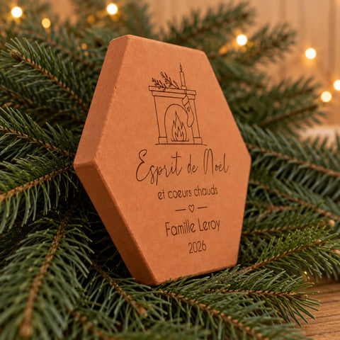 Tomette personnalisée « Esprit de Noël », Famille Leroy et cheminée gravés, vue de côté parmi des branches de sapin illuminées.