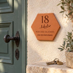 Personalised house plaque engraved with “18 rue des Oliviers”, “Aix-en-Provence” and a branch, fixed beside a green door near some keys.