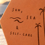 Gros plan sur les lettres Sun, sea & self-care, les vagues et les palmiers gravés.