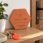 Tomette personnalisée « Notre premier chez-nous », Camille et Noé, cœur et adresse gravés, sur une console d’entrée près d’une plante et de clés à porte-clés souriant.