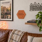 Tomette souvenir personnalisée Amsterdam, maisons, vélo, Emma et Tom et année gravés, fixée au mur au-dessus d’un canapé, près d’une affiche d’Amsterdam.