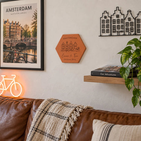 Tomette souvenir personnalisée Amsterdam, maisons, vélo, Emma et Tom et année gravés, fixée au mur au-dessus d’un canapé, près d’une affiche d’Amsterdam.