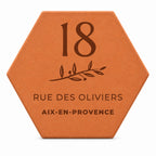 Personalised house plaque engraved with “18 rue des Oliviers”, “Aix-en-Provence” and a branch, on a white background.