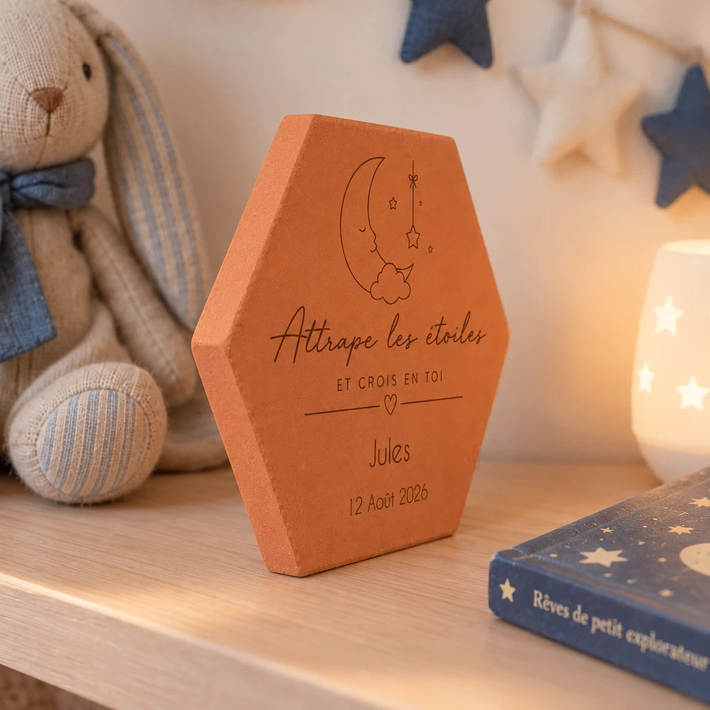 Tomette de naissance personnalisée Jules, lune et « Attrape les étoiles » gravés, vue de biais près d’un lapin en peluche et d’un livre bleu.