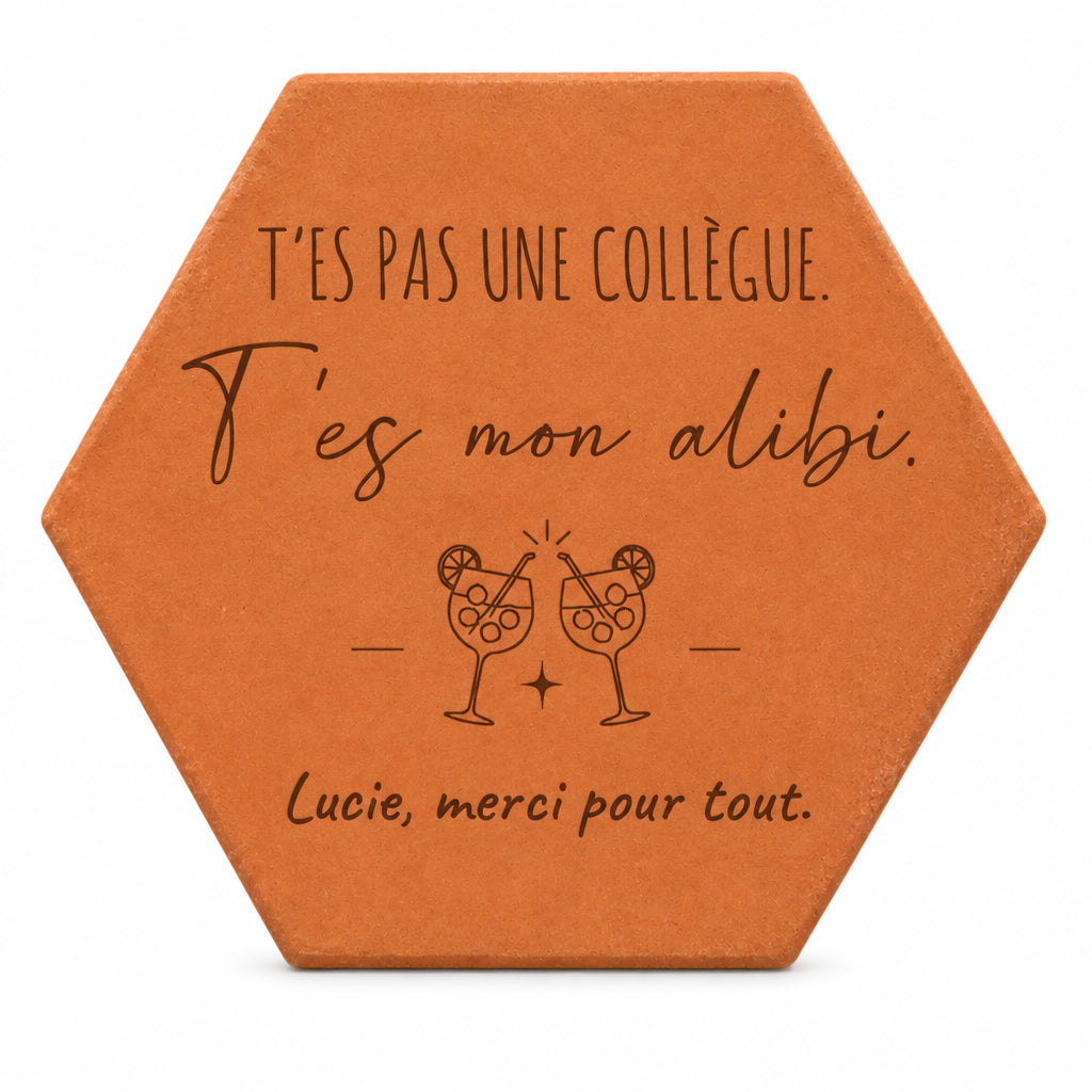 Pieza hexagonal de terracota grabada con «T'es pas une collègue. T'es mon alibi.» y dos copas de cóctel, sobre fondo blanco.