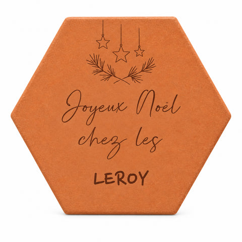 Tomette de Noël personnalisée « Joyeux Noël chez les Leroy », étoiles suspendues et rameaux de sapin gravés, sur fond blanc.