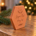Tomette « Joyeux Noël chez les Leroy » vue de profil sur une table en bois, tranche de terre cuite visible.