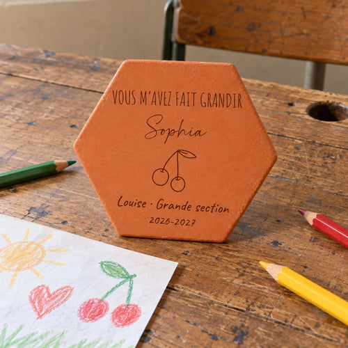 Pieza hexagonal de terracota «Cerezas» sobre un viejo pupitre con un dibujo y lápices.