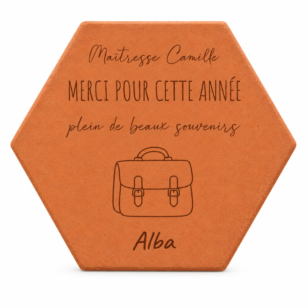 Pieza hexagonal de terracota grabada con una cartera, «Merci pour cette année», Alba y Maîtresse Camille, sobre fondo blanco.